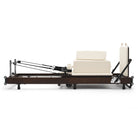 Reformer Pilates pieghevole Flexi, legno espresso fumé, rivestimento bianco latte – vista laterale con sitting box