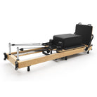 Reformer Pilates pieghevole Flexi, legno naturale, rivestimento nero – vista 3/4 con sitting box